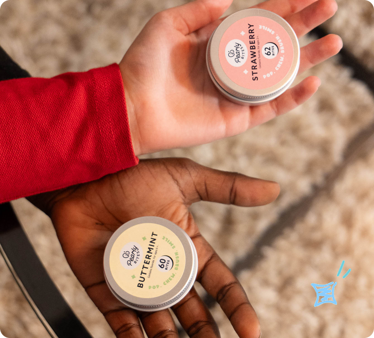 Two small round tins of pop candy are held in two hands. The top tin is labeled Strawberry and has a pink label; the bottom tin is labeled Buttermint and has a cream label.