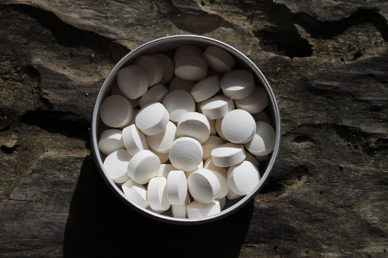 White round tablets piled in a small round metal tin, placed on a dark textured wooden surface.